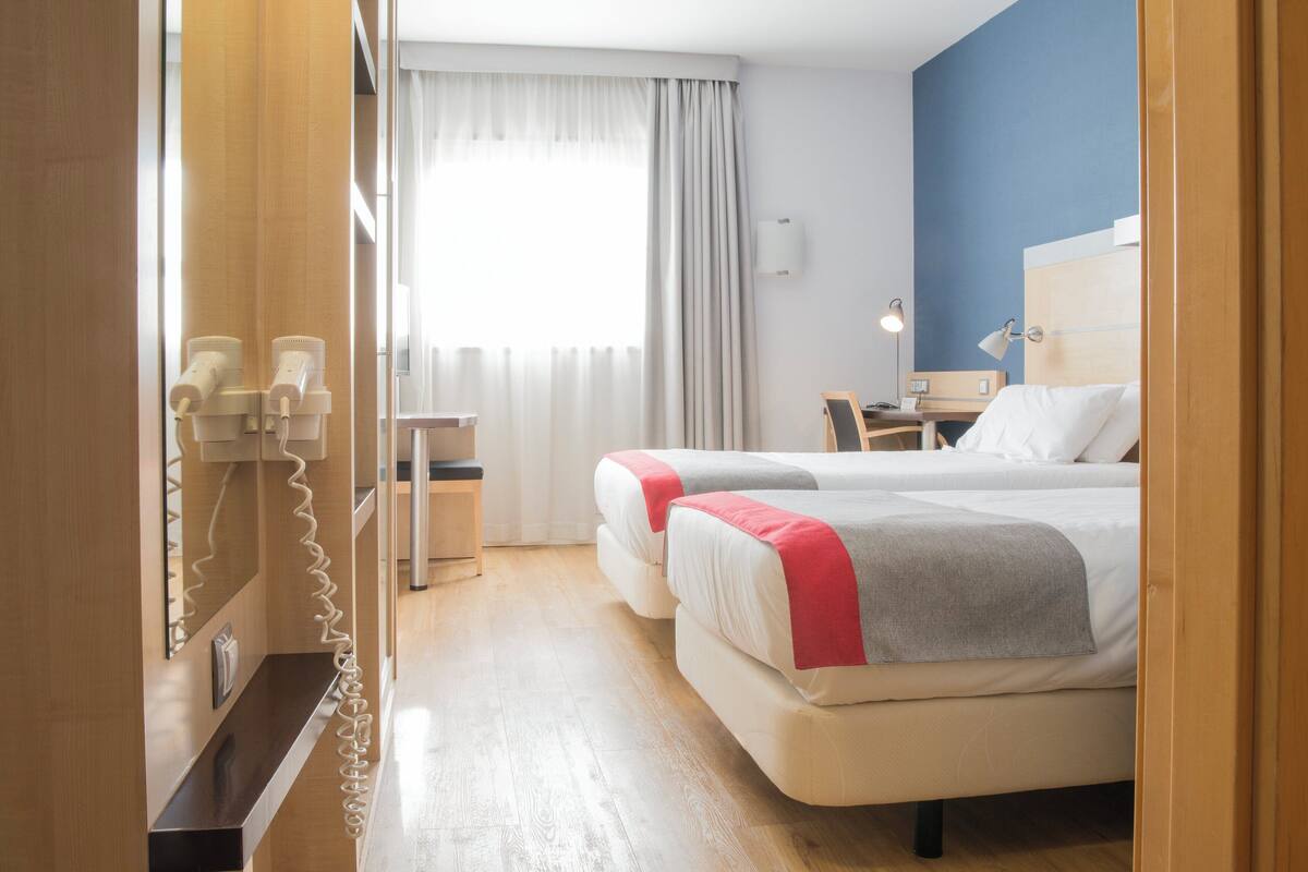 Hotellihuone, jossa on kaksi sänkyä, työpöytä, tuoli ja puhelin.