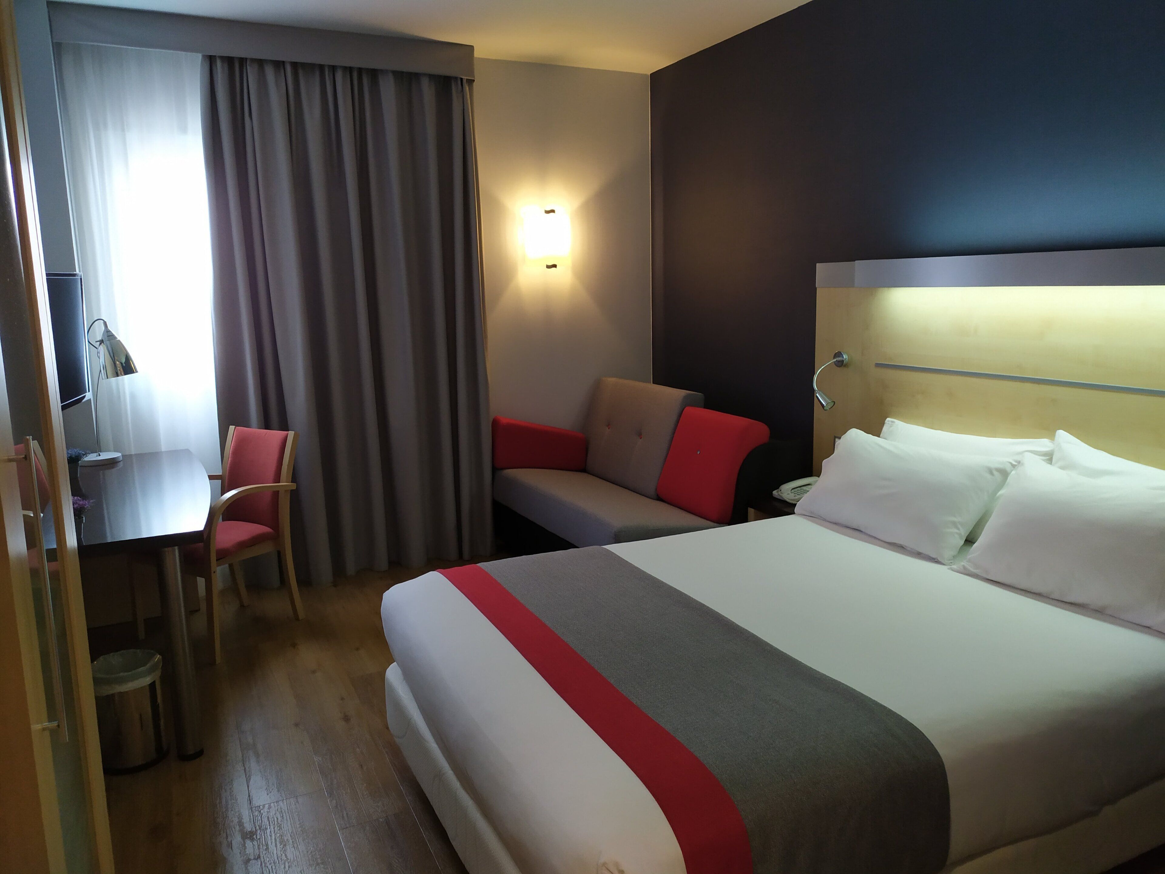 A hotel room with a bed, a desk, a chair, and a window with curtains.