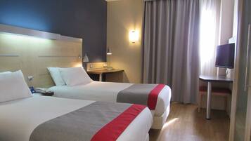 Habitación de hotel con dos camas, un escritorio, un televisor y una ventana con cortinas.