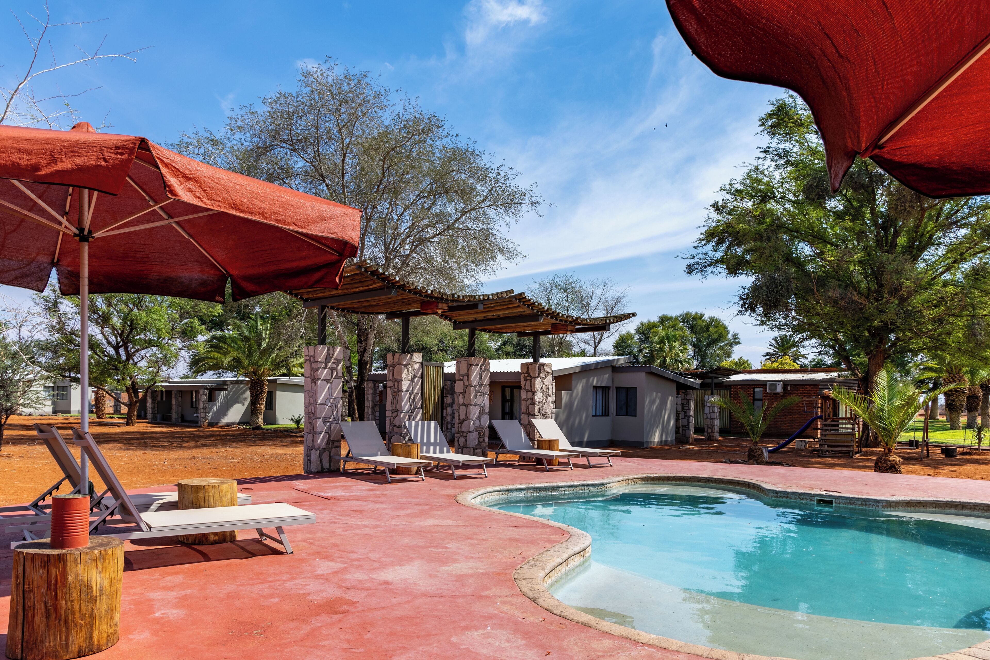 Una piscina con sillones de descanso y sombrillas, rodeada de pilares de piedra y árboles.