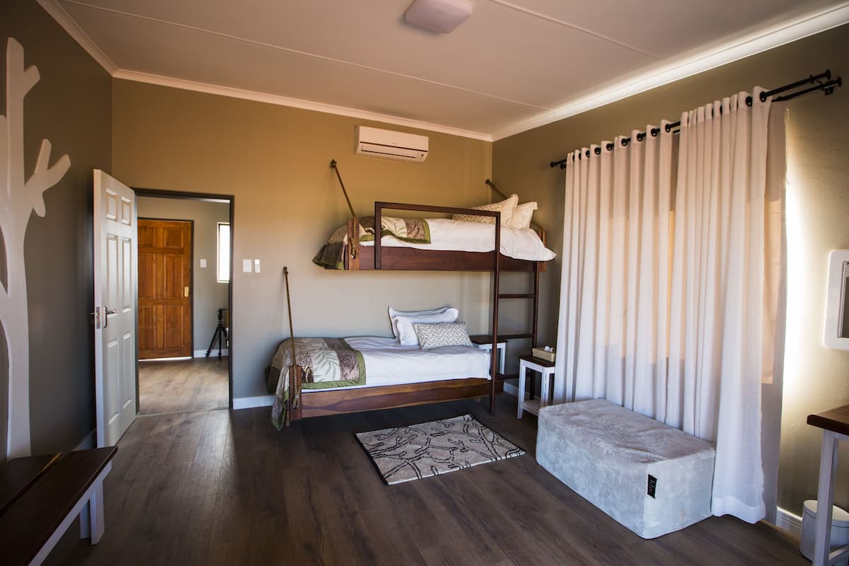 A bedroom with a bunk bed, a bedside table, a small bench, and a window with curtains.