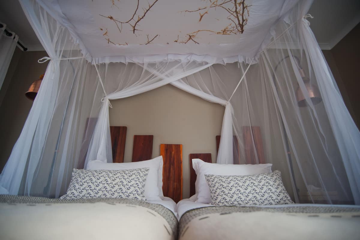 A bed with white bedding and patterned pillows, a wooden headboard, and a canopy with sheer white fabric.