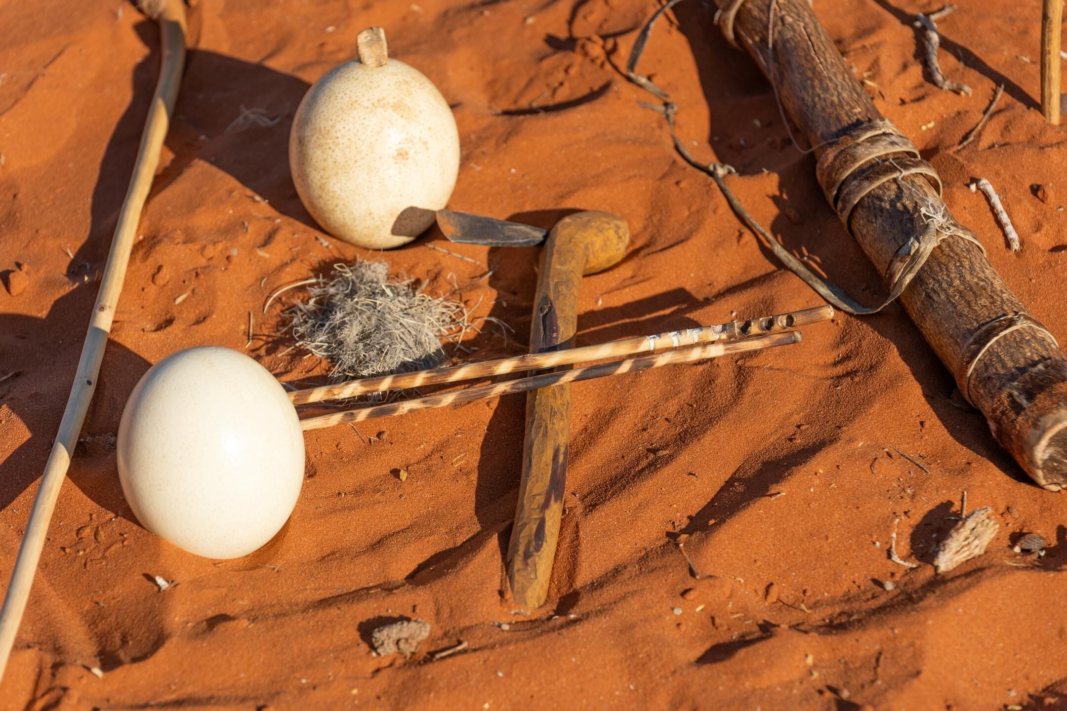 Une surface sablonneuse avec un objet sphérique blanc, un bâton en bois et un morceau de bois auquel est attachée une corde.