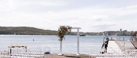 An outdoor wedding setup with white chairs arranged in rows, a white archway, and a floral decoration.