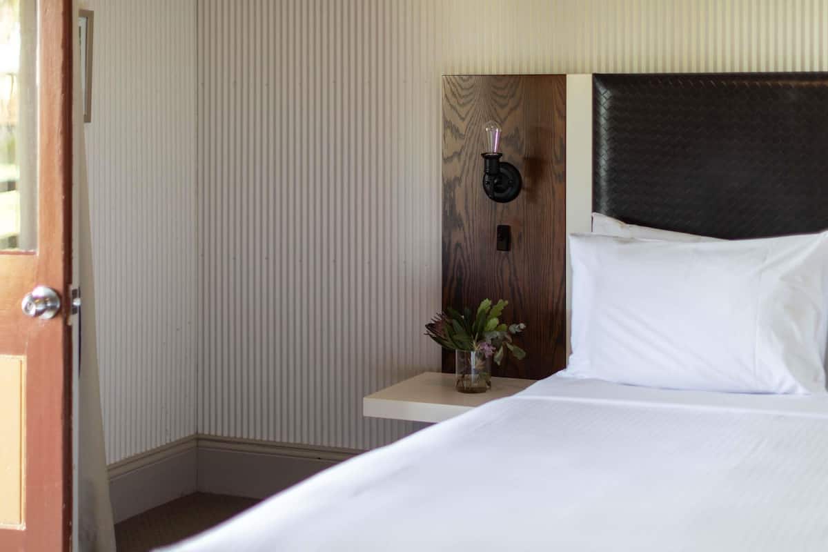 Ein Hotelzimmer mit einem Bett, einem Nachttisch mit Blumenvase, einer Wandleuchte und einer Tür.