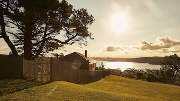 A house with a wooden fence, a large tree, and a view of a body of water during sunset.