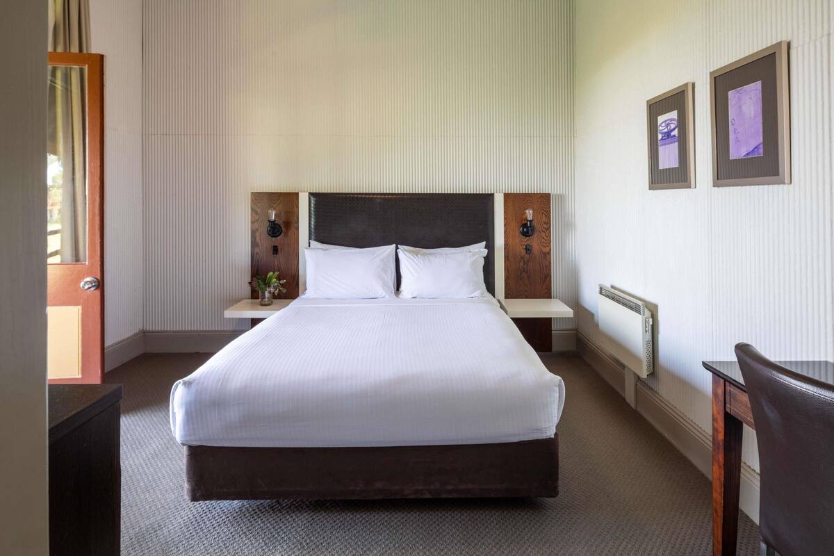 A neatly arranged hotel room with a large bed, bedside tables, a chair, and framed pictures on the wall.