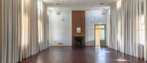 A spacious room with a wooden floor, white curtains, a fireplace, and a green door.