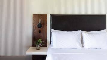 Habitación de hotel con una cama, una mesita de noche con un florero y una lámpara de pared, además de una pared con textura.