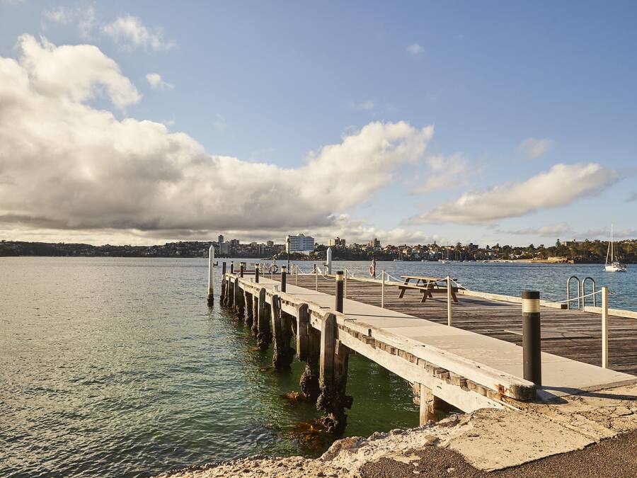 Un muelle se adentra en aguas tranquilas, con un paisaje urbano al fondo.