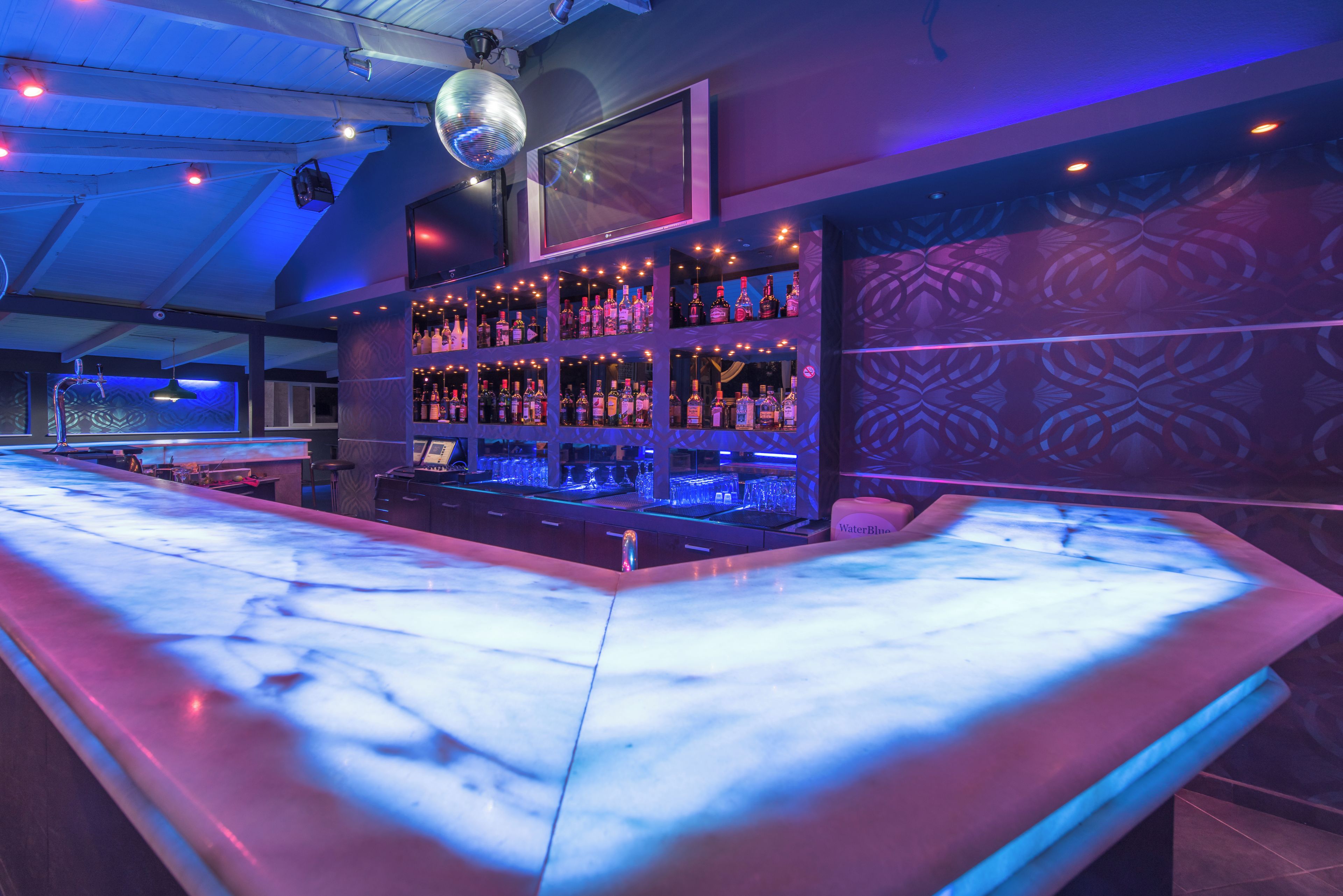 A bar area with a marble countertop, shelves of liquor bottles, and a disco ball.