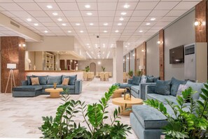 Un hall d'hôtel moderne avec des espaces de détente, un comptoir d'accueil et une cuisine en arrière-plan.