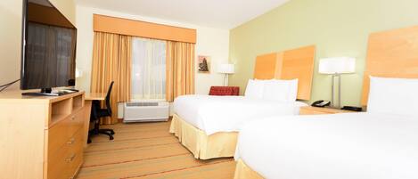 Habitación de hotel con dos camas, un escritorio, televisor y ventana con cortinas.