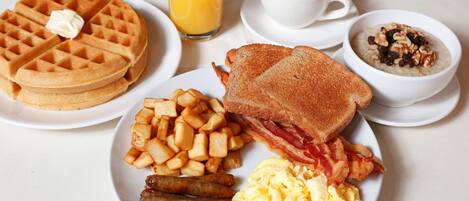 Un plato de desayuno con waffles, tostadas, tocino, salchichas, huevos revueltos y patatas ralladas.