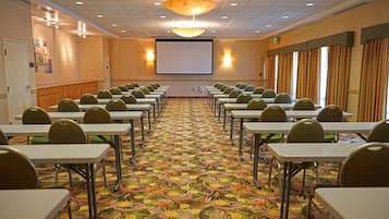 A conference room with rows of tables and chairs, a projector screen, and a patterned carpet.