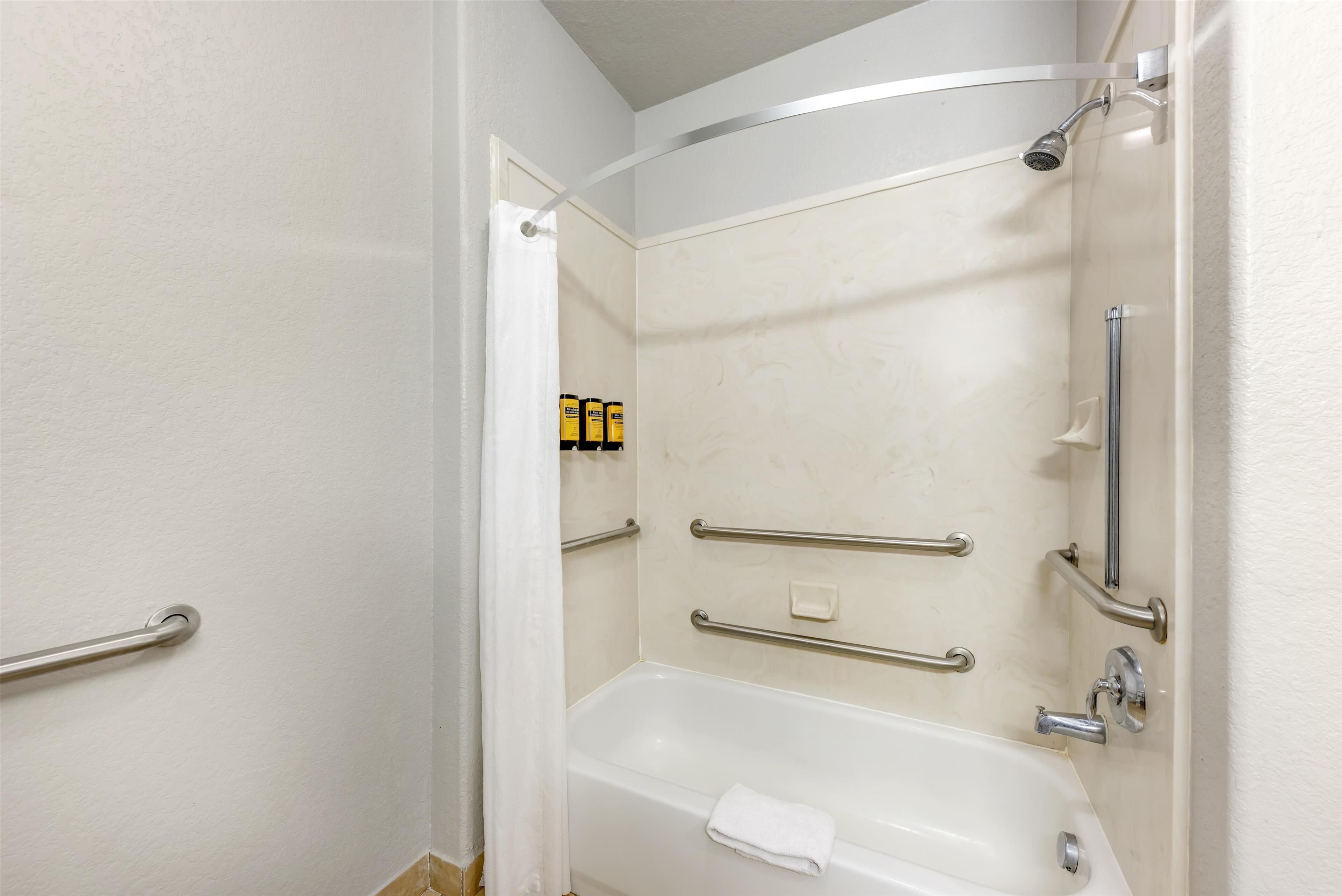 A bathroom with a bathtub, handrails, and a showerhead.