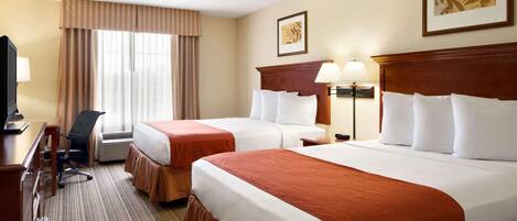A hotel room with two beds, a desk with a chair, a television, and a window with curtains.