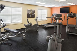 A gym with various exercise equipment, including treadmills and weight machines, and large windows with blinds.