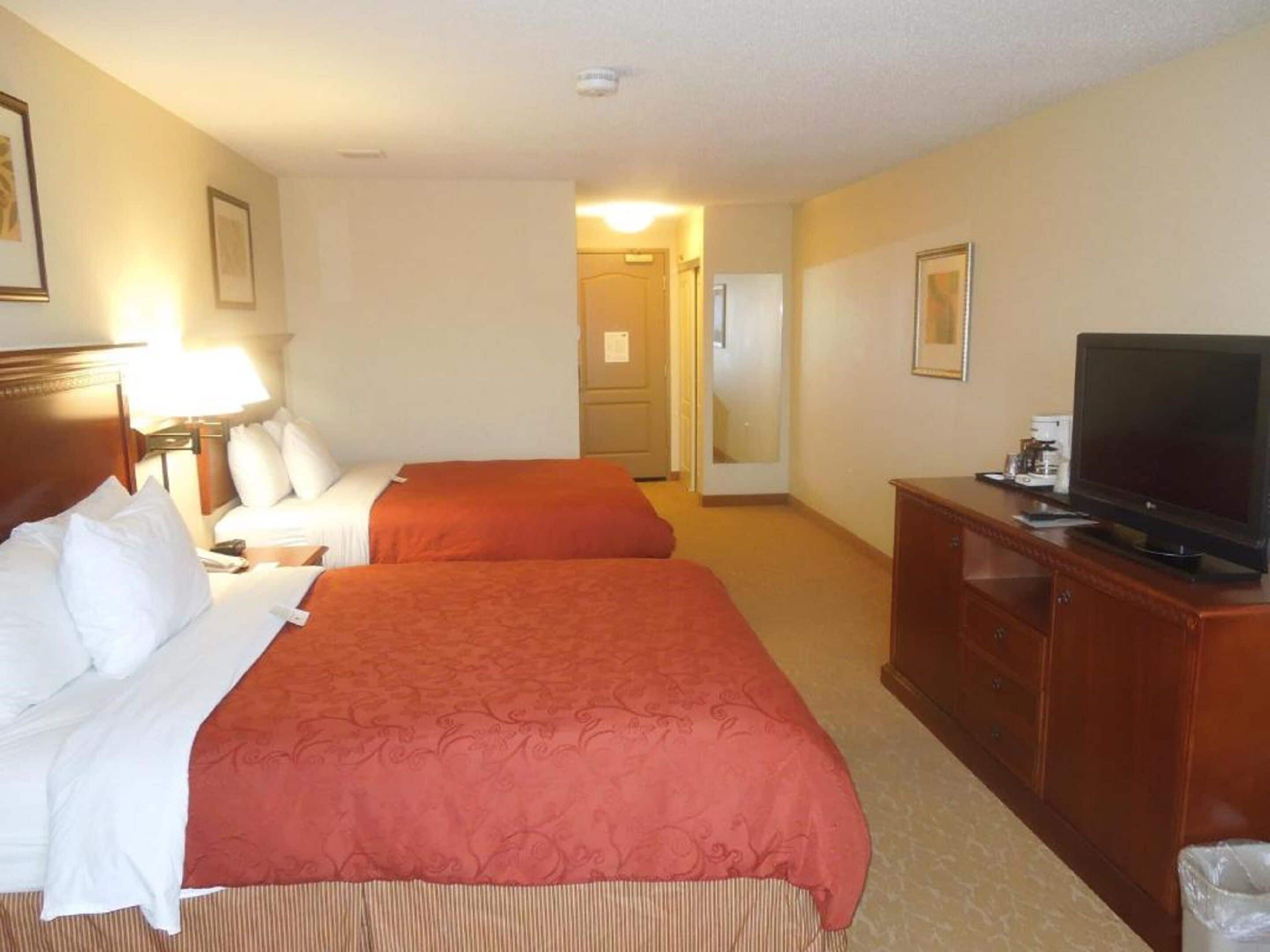 A hotel room with two beds, a television, a desk with a lamp, and a mirror.