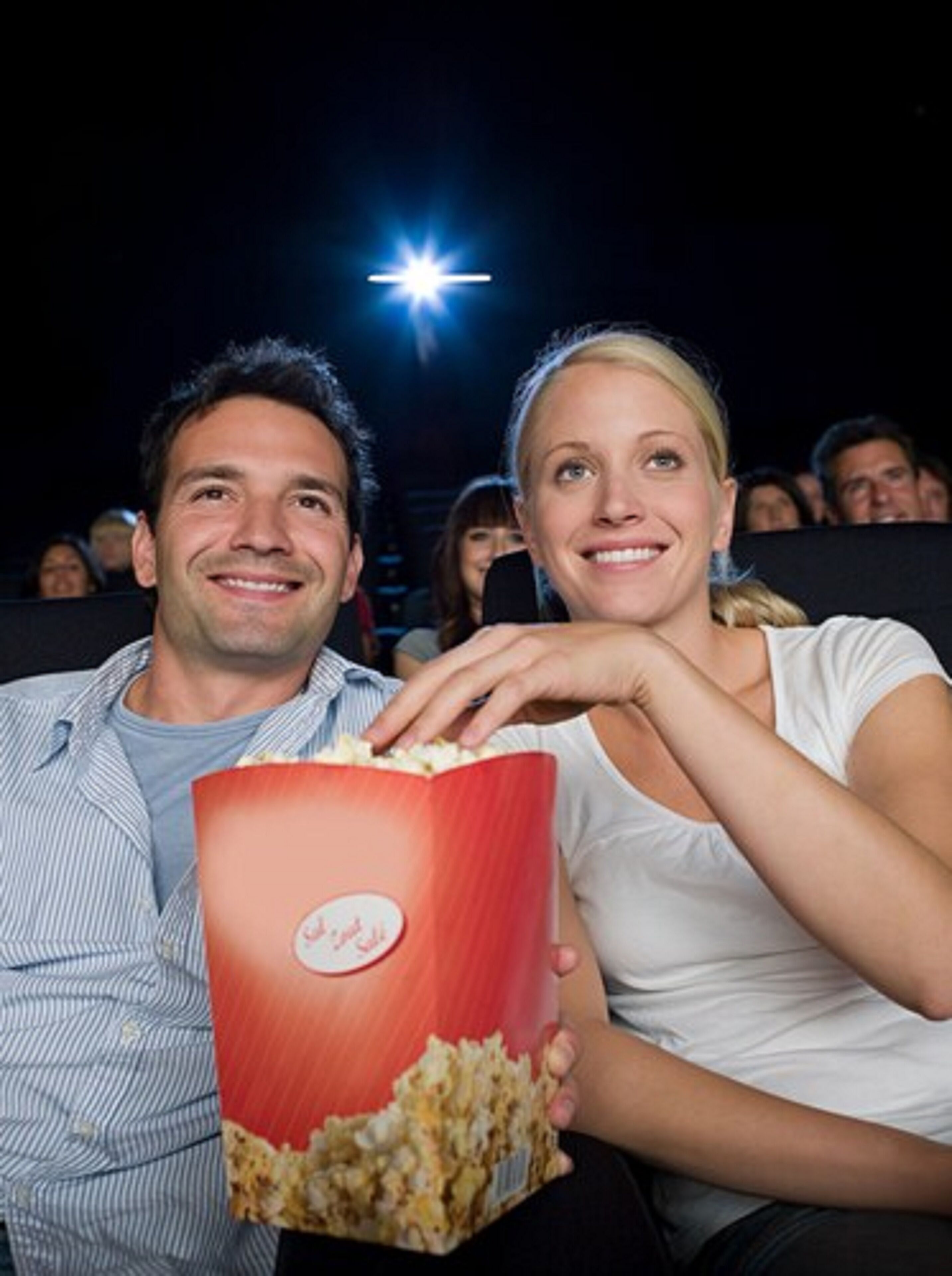 A couple seated in a movie theater with popcorn.