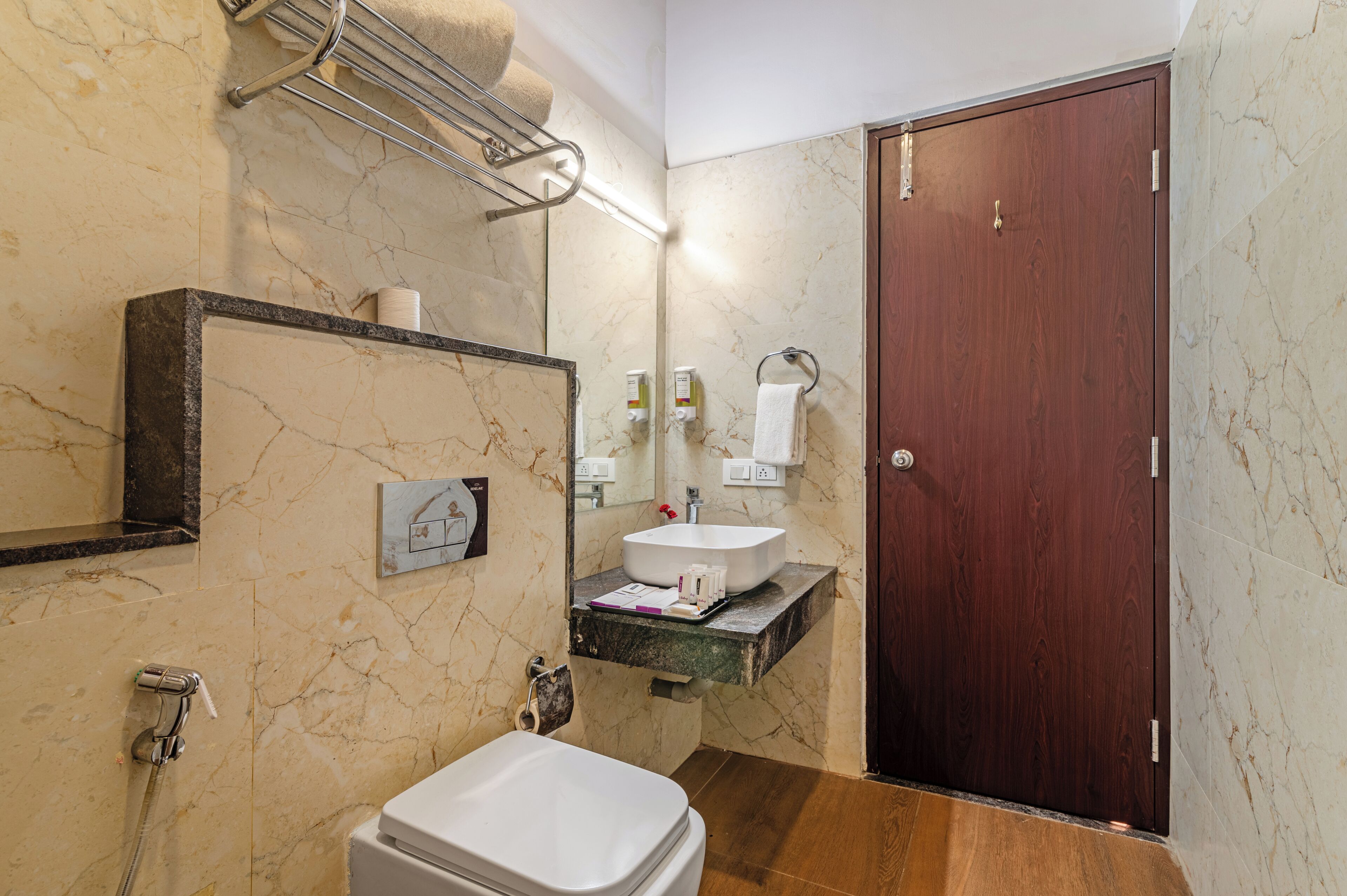A bathroom with a marble wall, a wooden door, a sink, and a toilet.