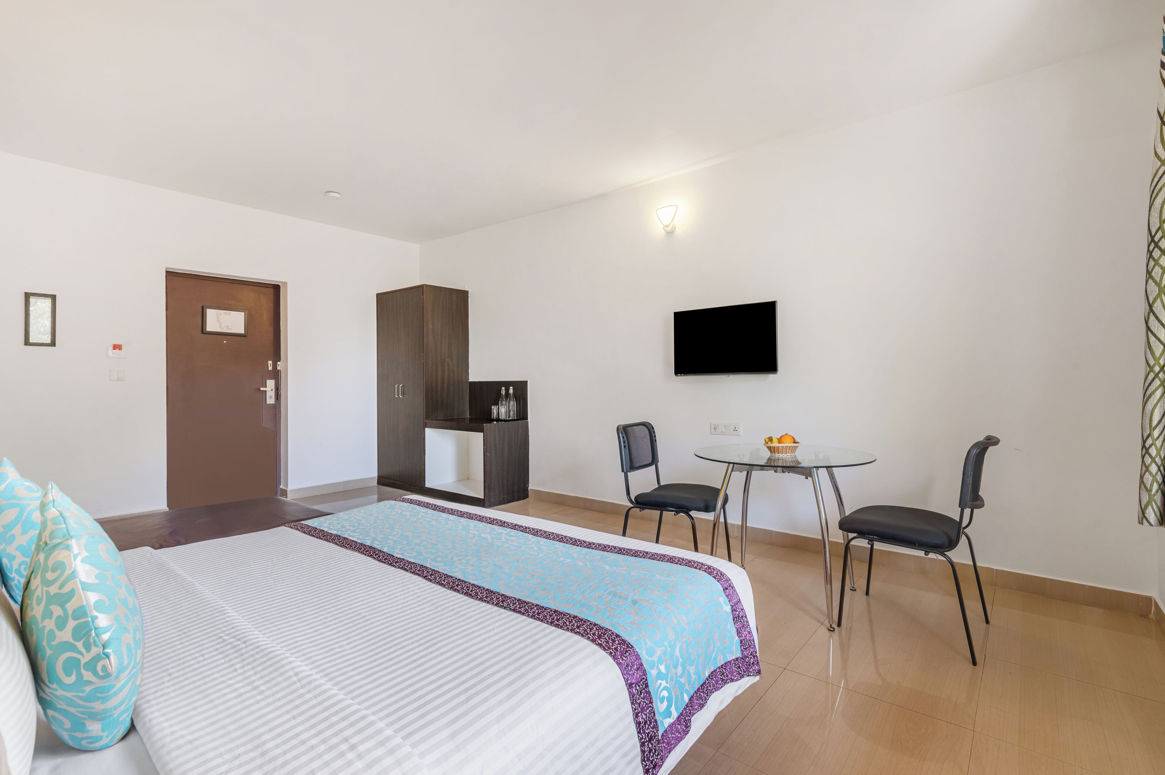 Ein Hotelzimmer mit einem Bett, einem Schreibtisch mit Stuhl, einem Fernseher und einer Tür.