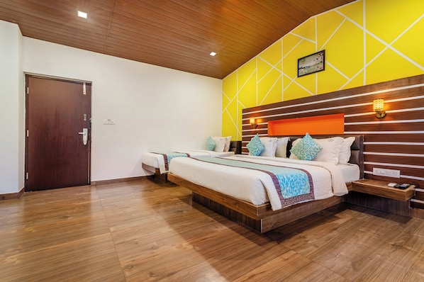 A hotel room with a wooden ceiling, a yellow accent wall, and a large bed with multiple pillows.