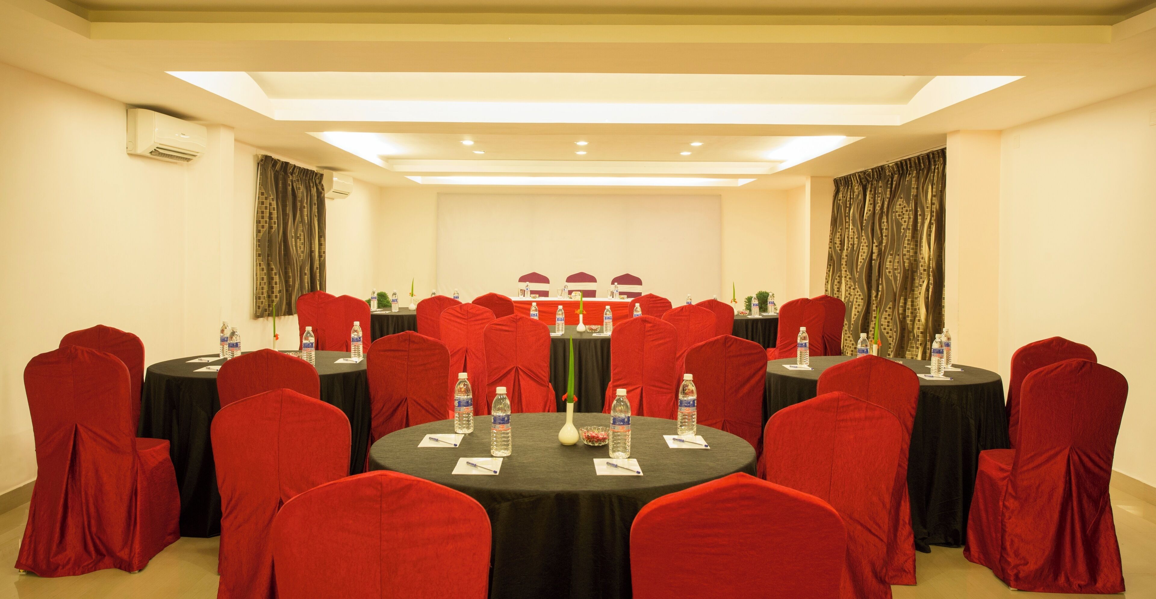 A conference room with round tables, red chairs, and black tablecloths.