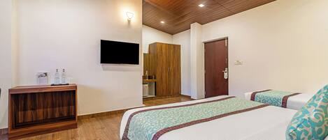 Ein Hotelzimmer mit zwei Betten, einem Holzkonsolentisch, einem an der Wand montierten Fernseher und einer Holzbalkendecke.