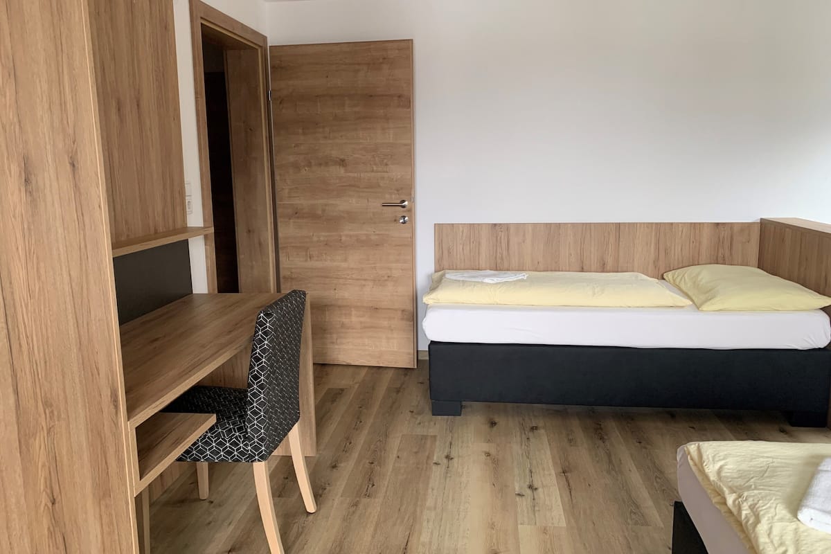 Een compacte slaapkamer met een houten garderobe, een enkel bed met hoofdeinde, een klein bureau met stoel en een houten vloer.