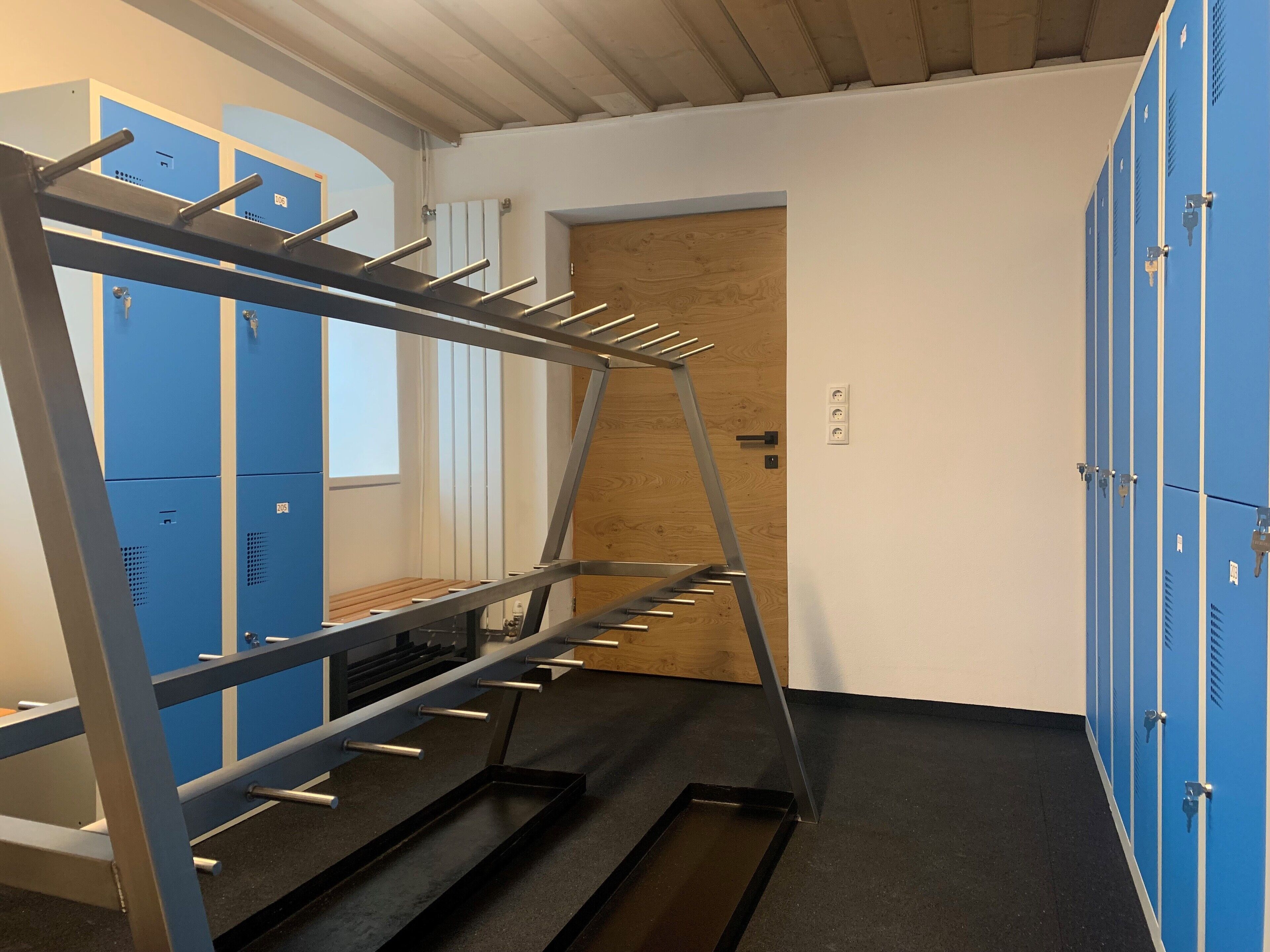 Una habitación con un perchero metálico, taquillas azules y una puerta de madera.