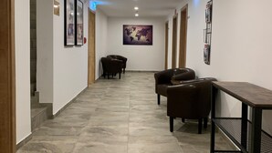 A hallway with a tiled floor, framed pictures on the walls, a world map, and a seating area with chairs and a table. - Gästehaus Elisabeth (Tulfes)