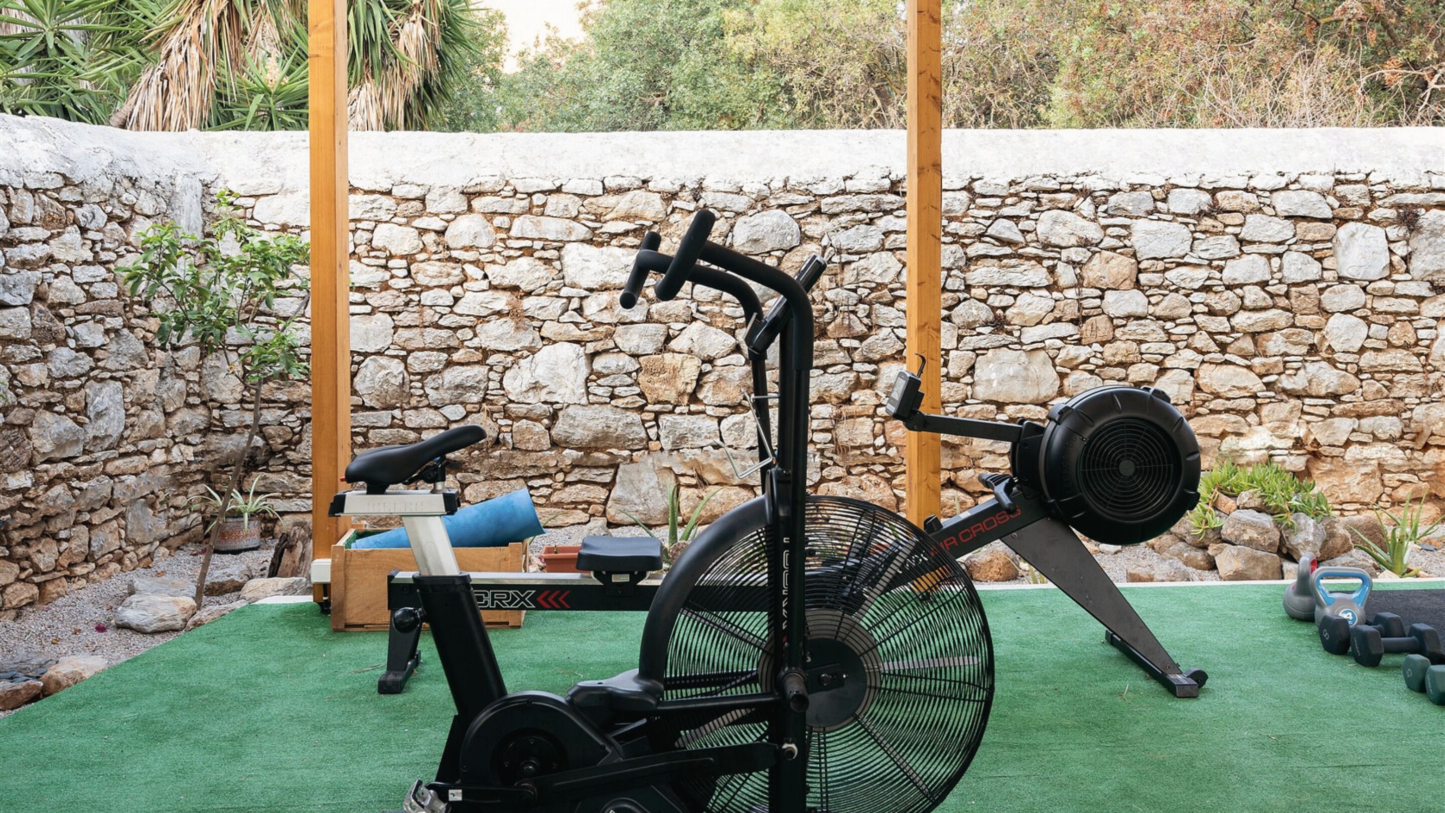 An outdoor exercise area with a stationary bike, a bench, and weights.