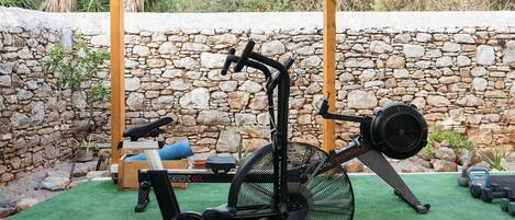 An outdoor exercise area with a stationary bike, a bench, and weights.