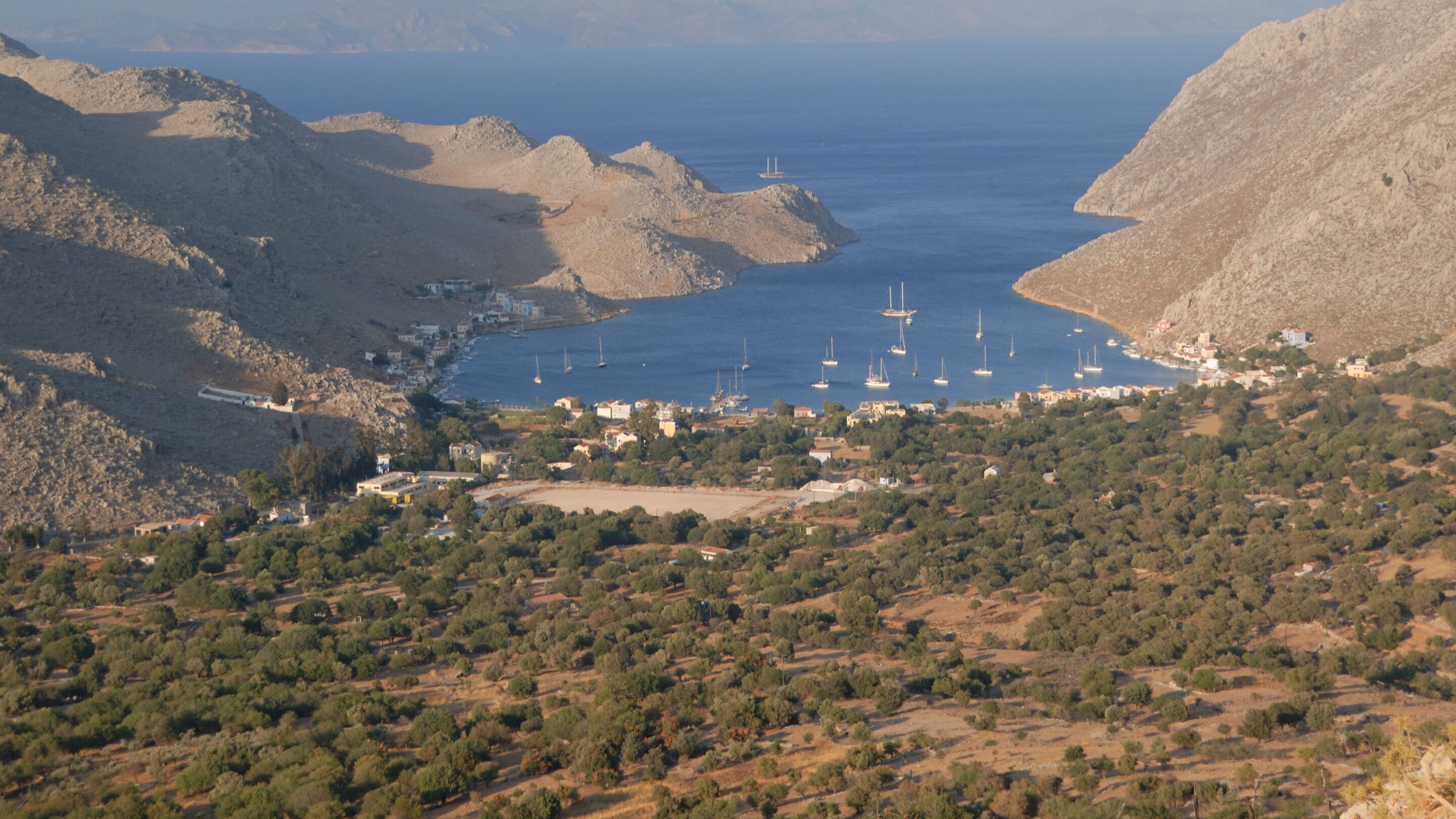 A coastal town with a marina, surrounded by hills and dense vegetation.