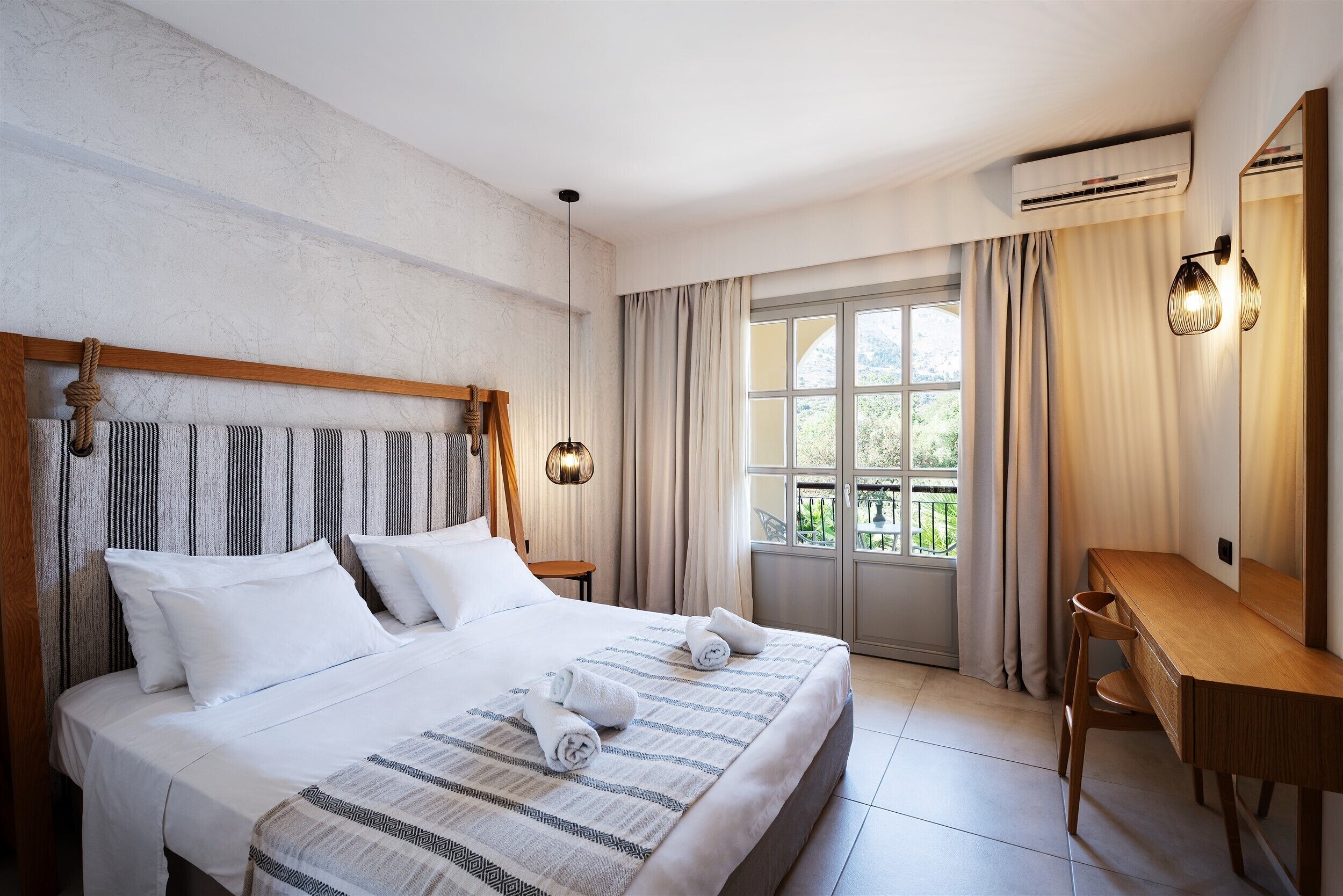 Quarto de hotel com uma cama grande, uma escrivaninha de madeira e vista para o exterior através de uma janela ampla.