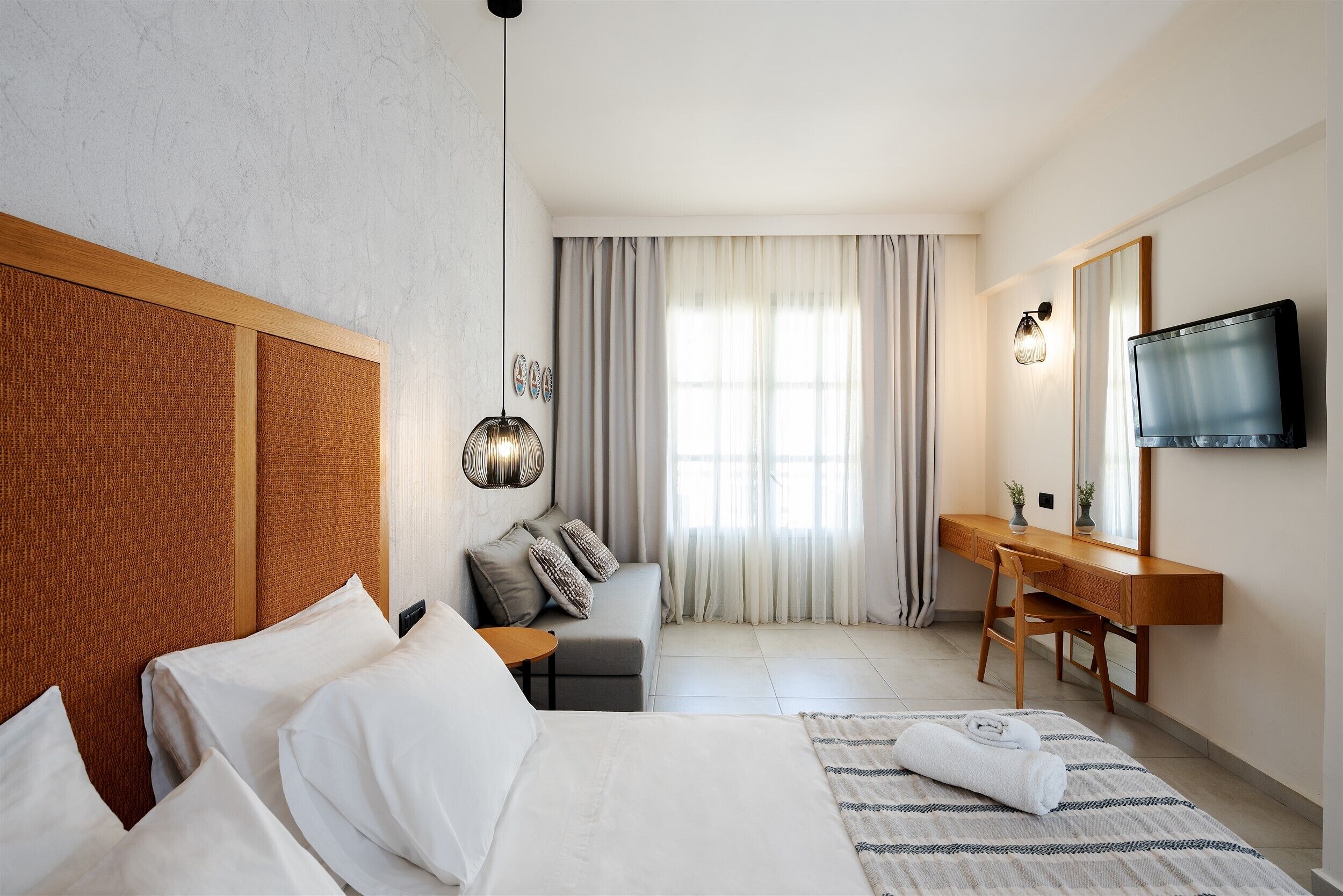 Quarto de hotel com cama, escrivaninha, cadeira, televisão e janela com cortinas.