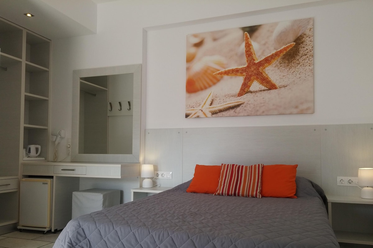 Un dormitorio con cama, escritorio, espejo y un cuadro en la pared con una estrella de mar.