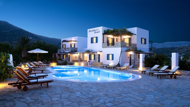A modern hotel with a swimming pool, lounge chairs, and a mountainous backdrop.
