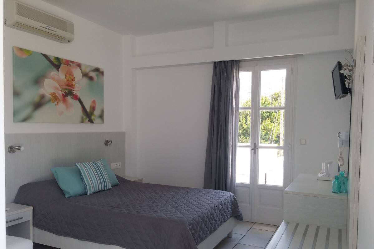 Un dormitorio con cama, una mesita de noche, cortinas en una ventana y aire acondicionado instalado en la pared.