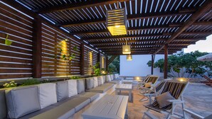 An outdoor seating area with a wooden pergola, cushioned benches, and tables.