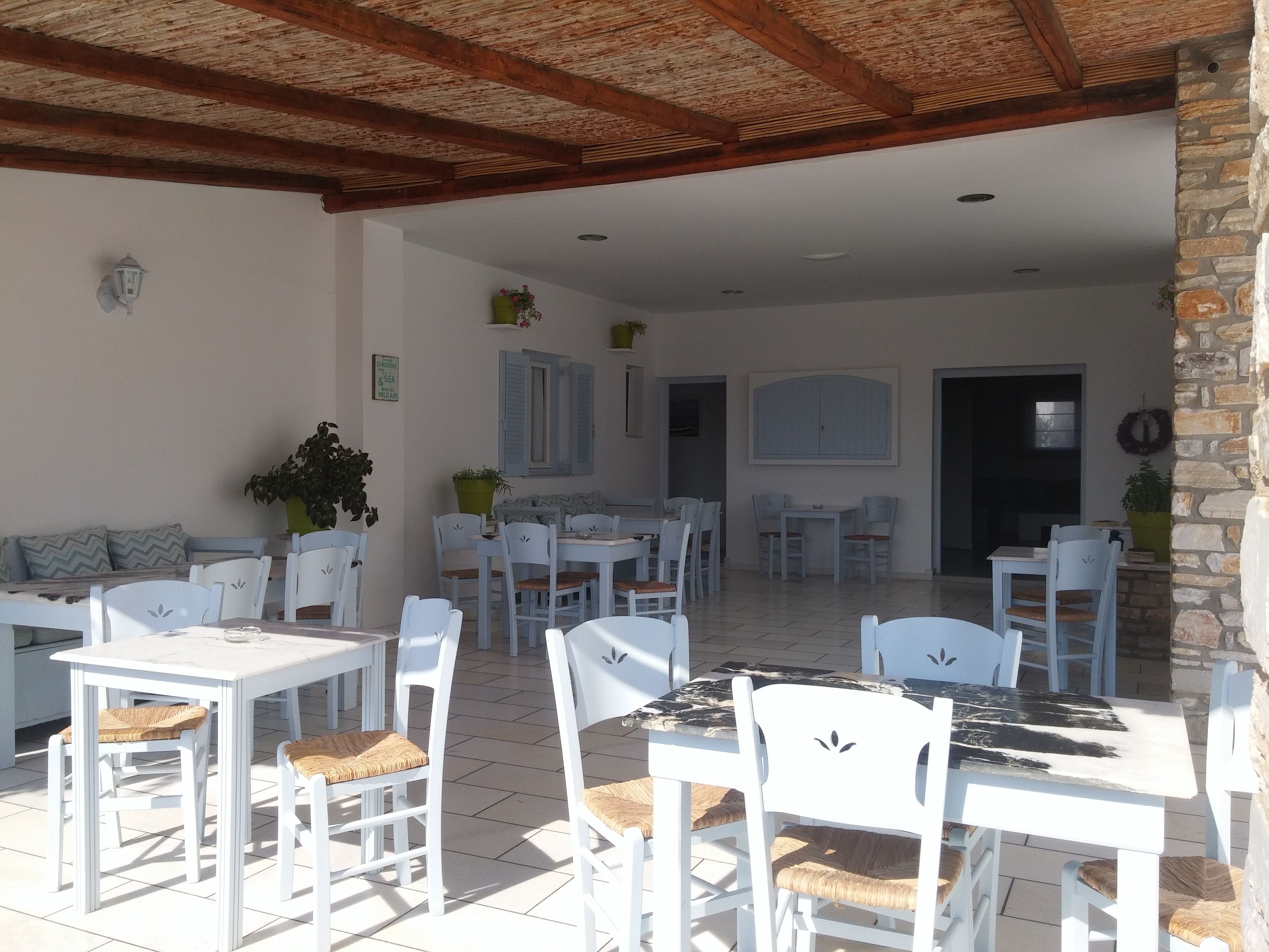 An outdoor patio with white tables and chairs, a stone wall, and a wooden ceiling.