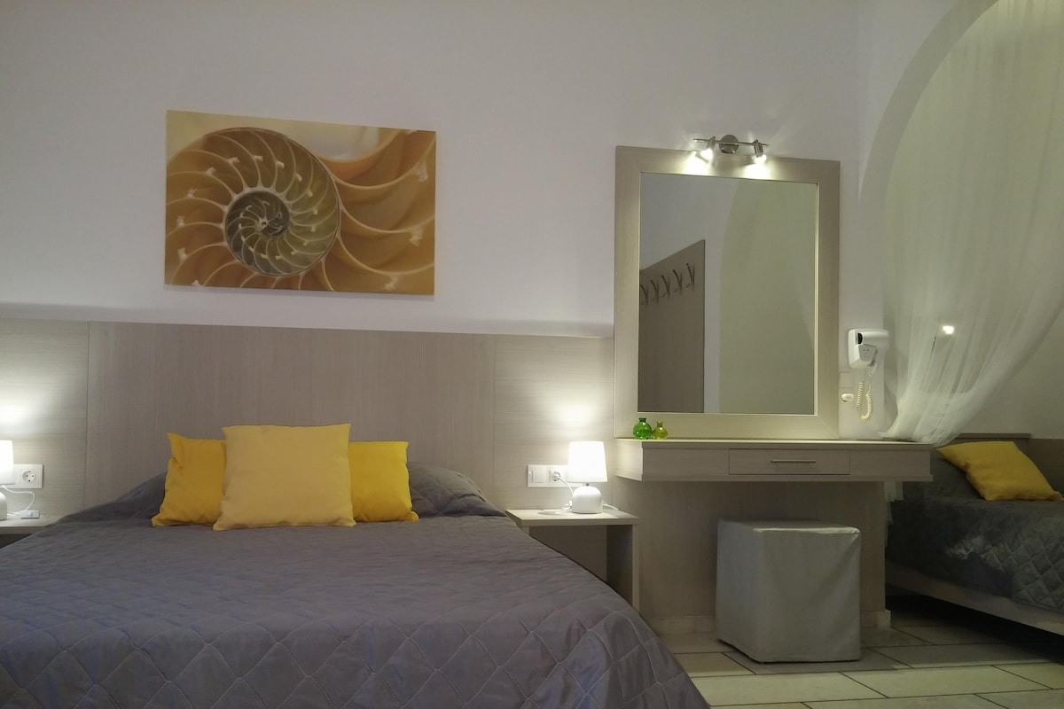 Habitación de hotel con una cama grande, una mesita de noche con lámpara, un tocador con espejo y un pequeño cubo de basura.