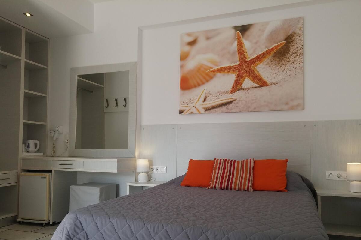 Un dormitorio con cama, escritorio, espejo y un cuadro en la pared con una estrella de mar.