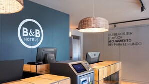 Un comptoir d’accueil d’un hôtel de type « bed and breakfast », doté d’un terminal de paiement numérique, d’un espace salon et d’un mur orné d’une citation inspirante.