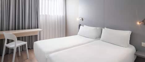 Habitació d'hotel amb dos llits, una taula i una cadira.