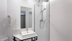 Une salle de bain moderne avec un lavabo blanc, un miroir et une douche équipée d’un pommeau de douche à main.