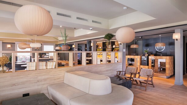 Un hall d’hôtel moderne comprenant un comptoir d’accueil, un espace salon et un grand comptoir d’accueil en bois.