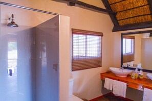 Un baño con ducha de vidrio, tocador de madera, un espejo grande y una ventana con persianas.