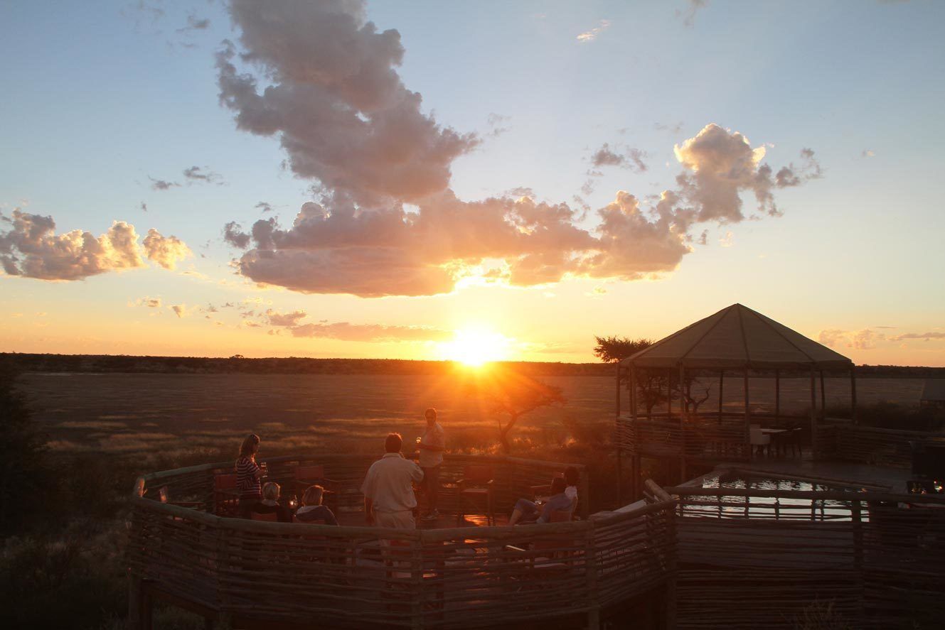 Vista del atardecer desde una terraza de madera con un pabellón, rodeado de campos abiertos.